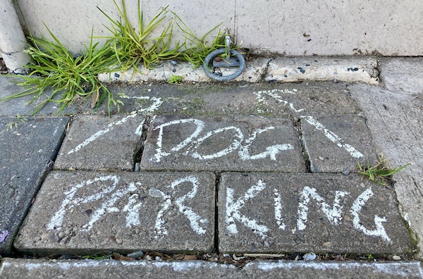 The words "Dog Parking" written in chalk on the pavement pointing to a metal hoop