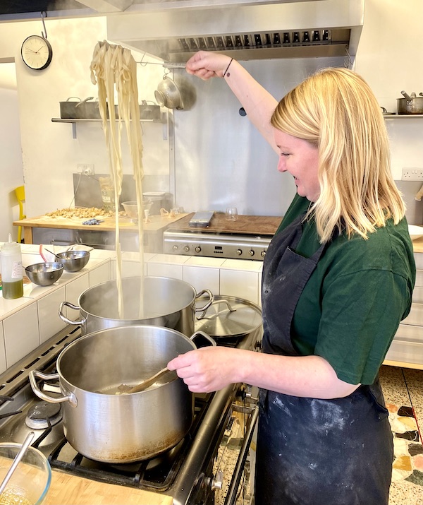 Martha ladling a large clump of pasta over a pot in the Loaf cookery school.