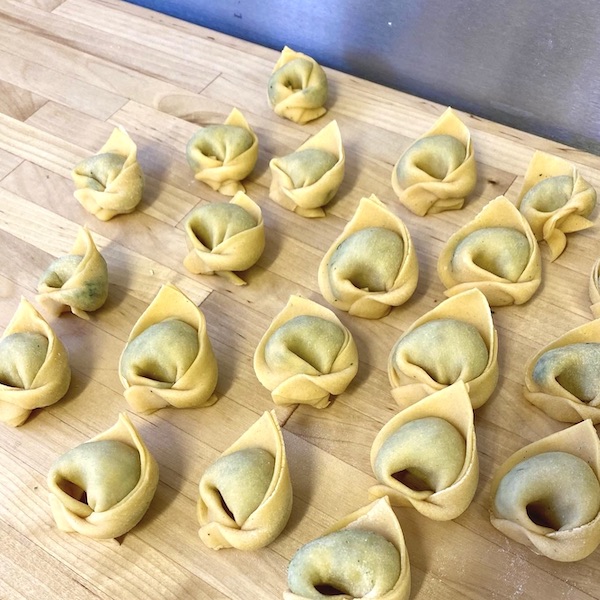 Some freshly made tortellini shells on a wooden kitchen surface, waiting to be cooked.